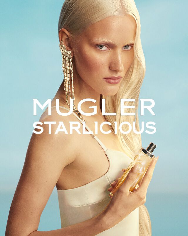 Mugler Starlicious Les Eaux Gourmandes campaign banner with model in pale yellow dress holding Pineapple Musk bottle against a soft blue sky.