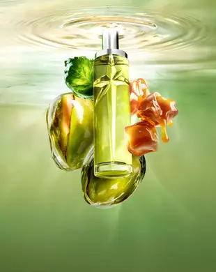New Starlicious Pistachio Praline still life image featuring the slender bottle surrounded by its key ingredients: a patchouli leaf, whole pistachios, and dripping caramel cubes, all set against a luminous green rippling water background.