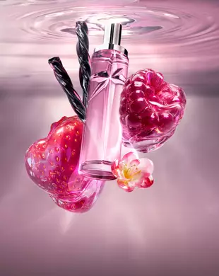 New Starlicious Berry Licorice still life featuring the slender glass bottle surrounded by its key ingredients: a glossy red strawberry, a vibrant raspberry, a delicate pink flower, and twisted black licorice sticks, all set against a soft pink rippling water background.