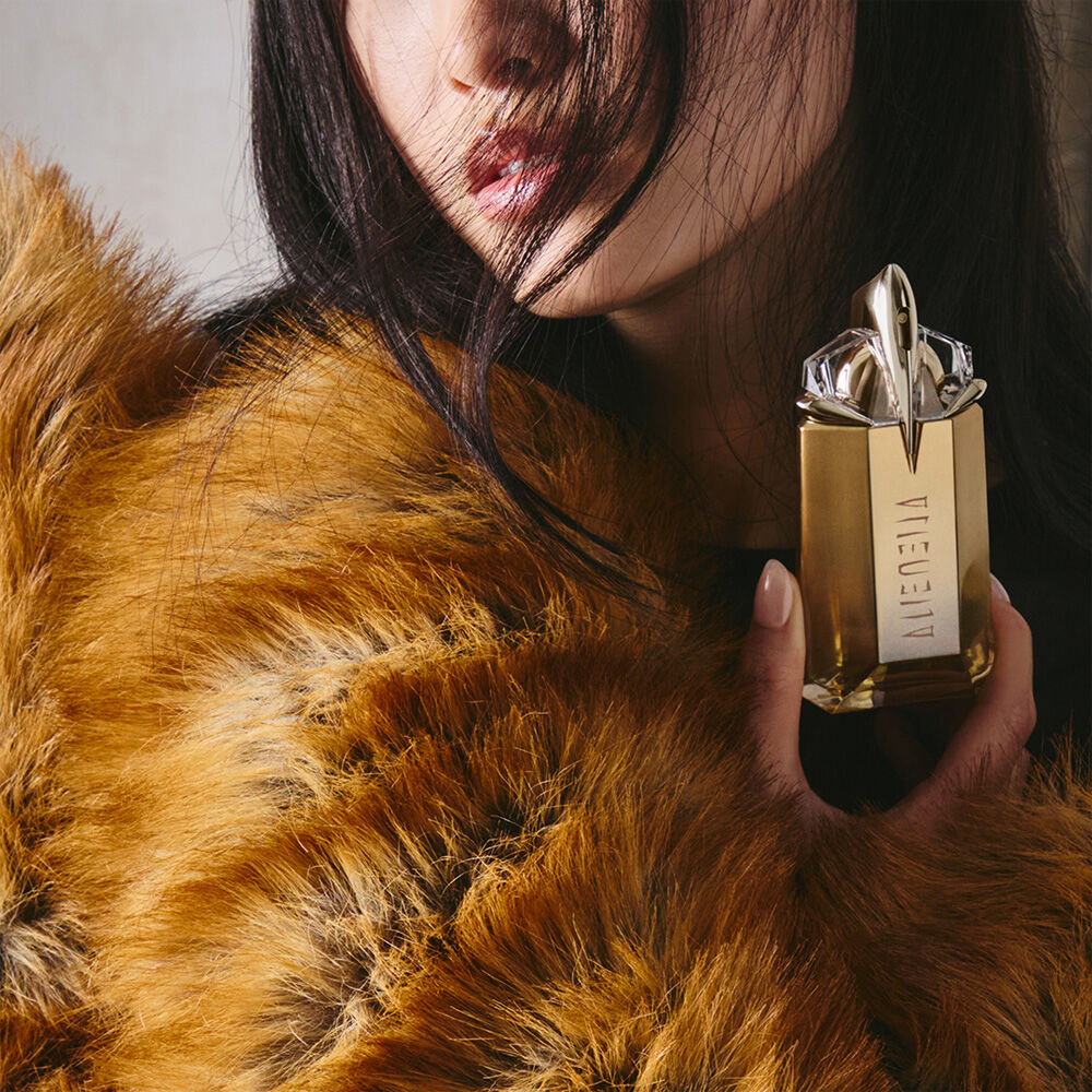 Model in a brown faux fur coat holding an Alien Goddess perfume bottle​