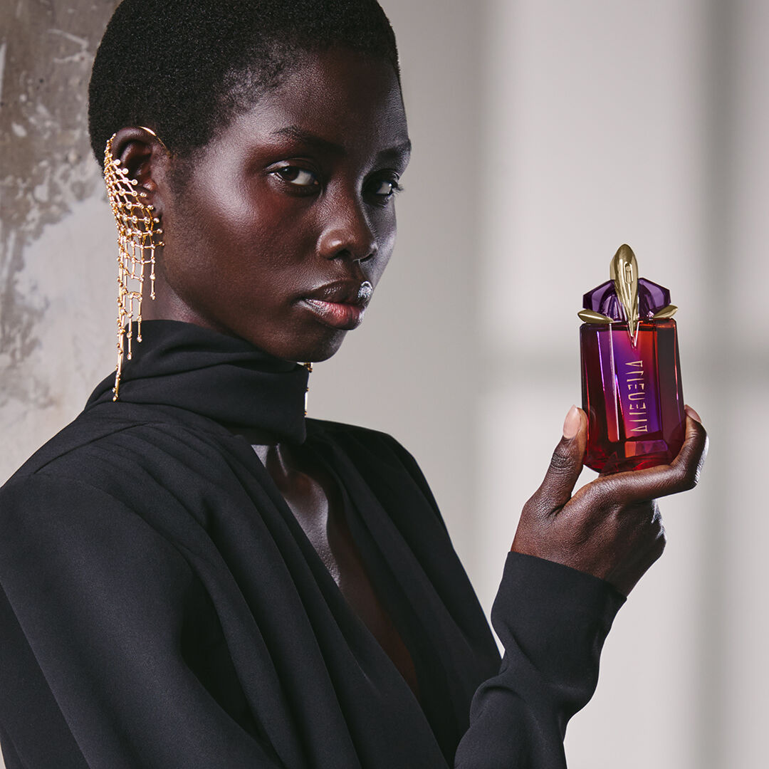 Model in black outfit holding Alien Hypersense perfume bottle​