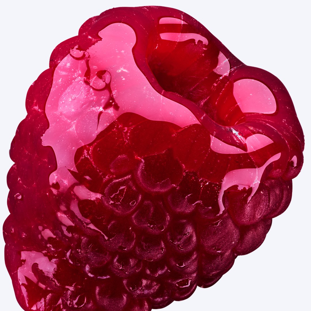 Extreme close-up of a raspberry coated in a translucent dark red glossy liquid against a light background