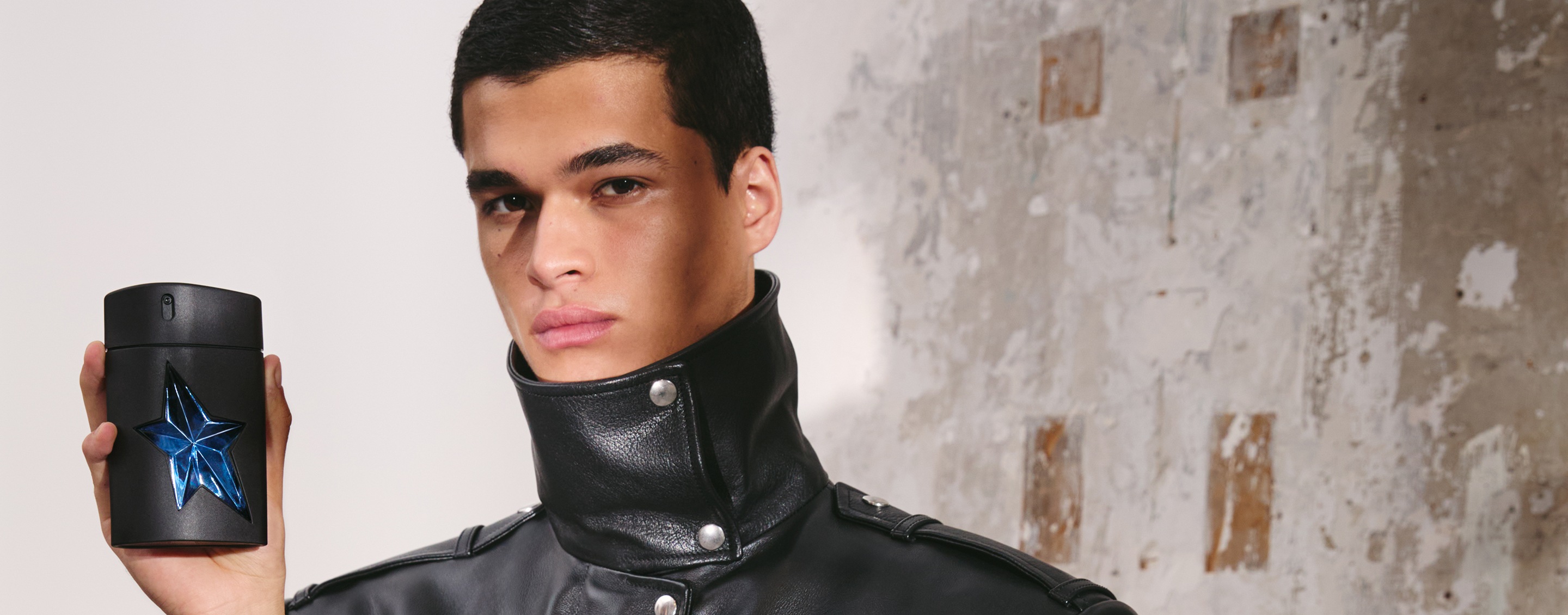 Person holding black A*Men Mugler bottle against textured wall