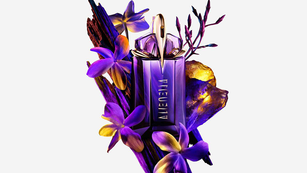 Mugler Alien perfume bottle surrounded by purple flowers and textured wood