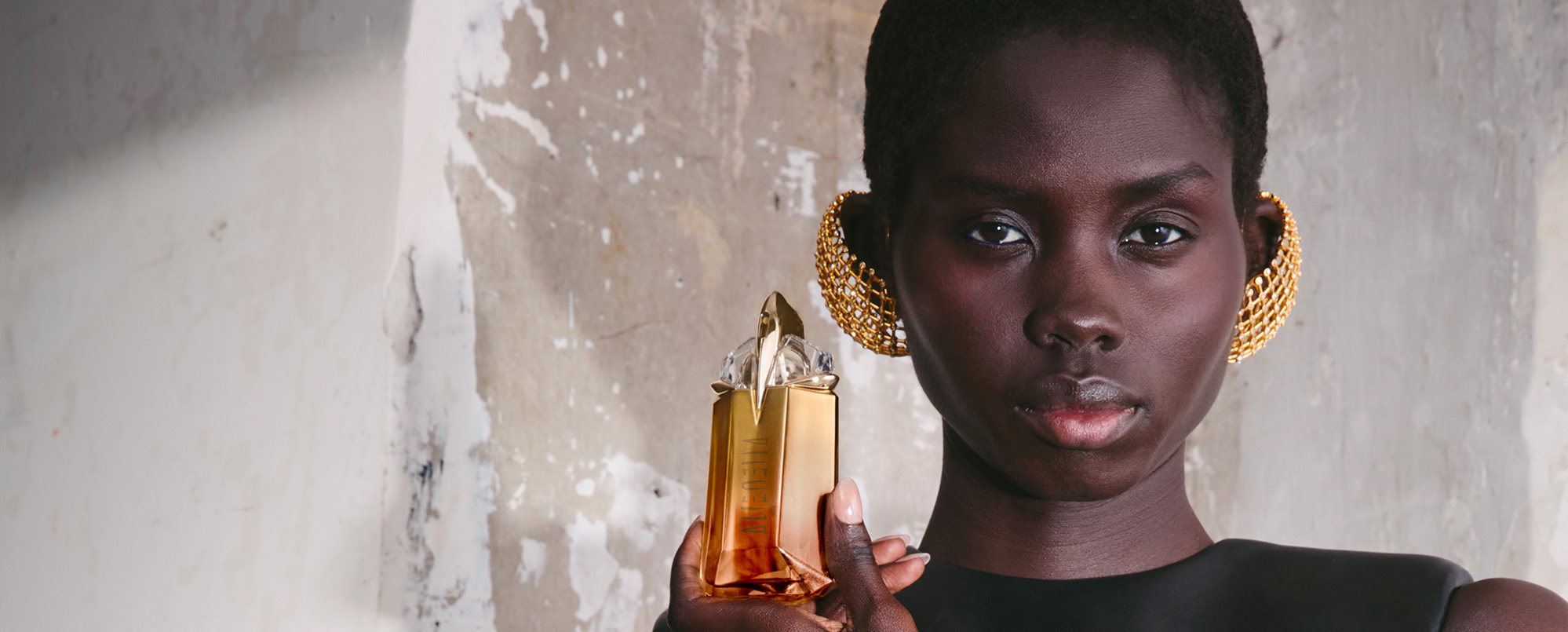 Elegant Black model holding Mugler Alien Goddess Intense golden talisman bottle, luxury fragrance campaign lifestyle shot