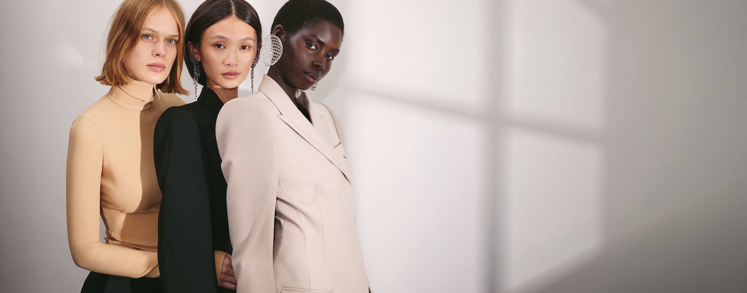 Three people in neutral tailored outfits posing together in soft light