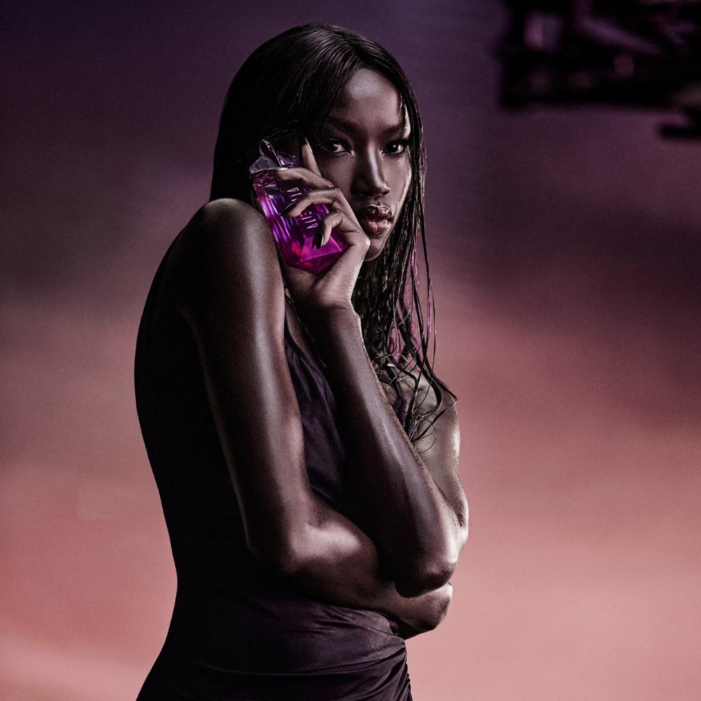 Alien Pulp by Mugler campaign portrait with model Anok Yai holding the fragrance bottle against a purple sunset backdrop