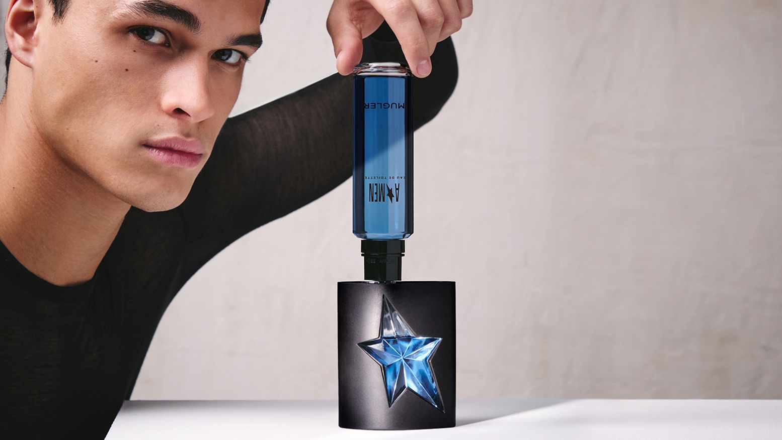 Hand refilling black A*Men Mugler bottle with blue refill bottle
