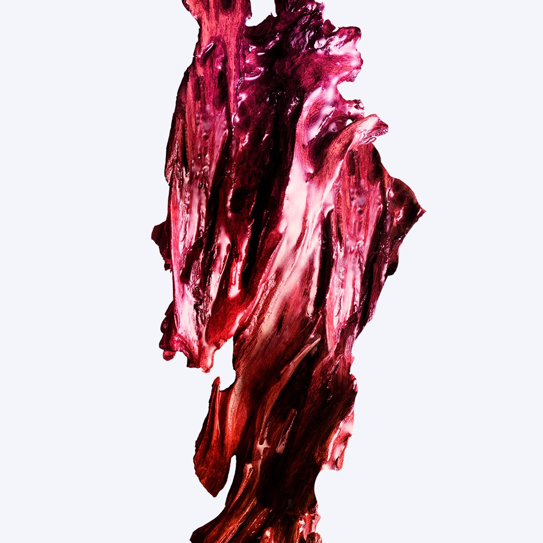 Abstract macro smear of deep crimson and raspberry-toned fragrance ingredient against a pale blue
background